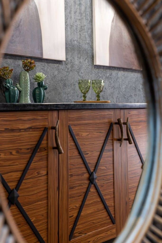 Through oval shaped hole view of glasses with ornament on tray against vases with decorative plants on table in house
